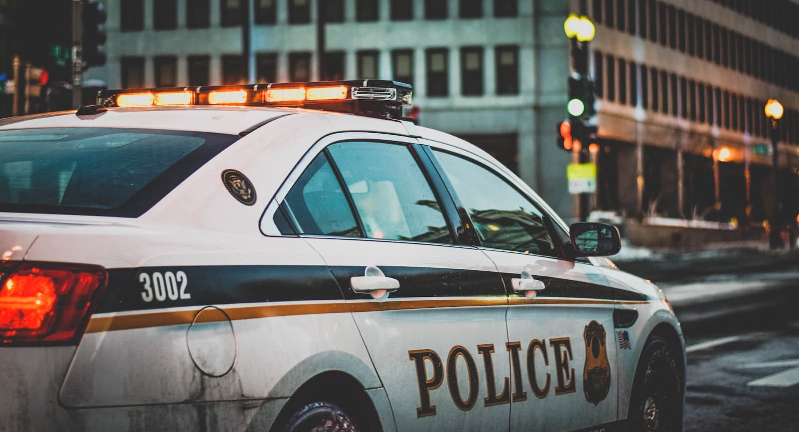 Police car 3002 parked on city street at dusk with illuminated buildings in background