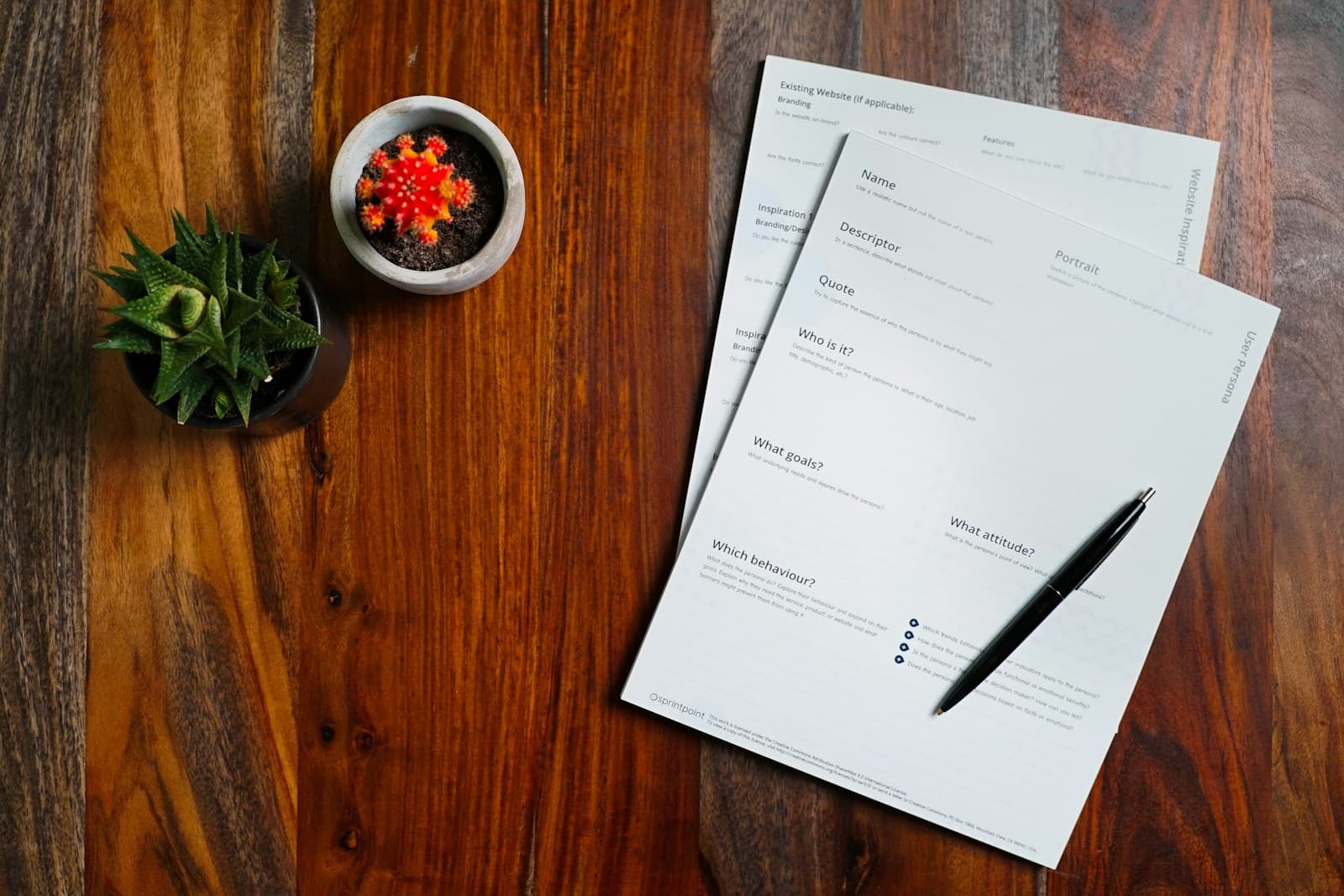 Documents with pen on wooden desk alongside small plant and bowl of red berries